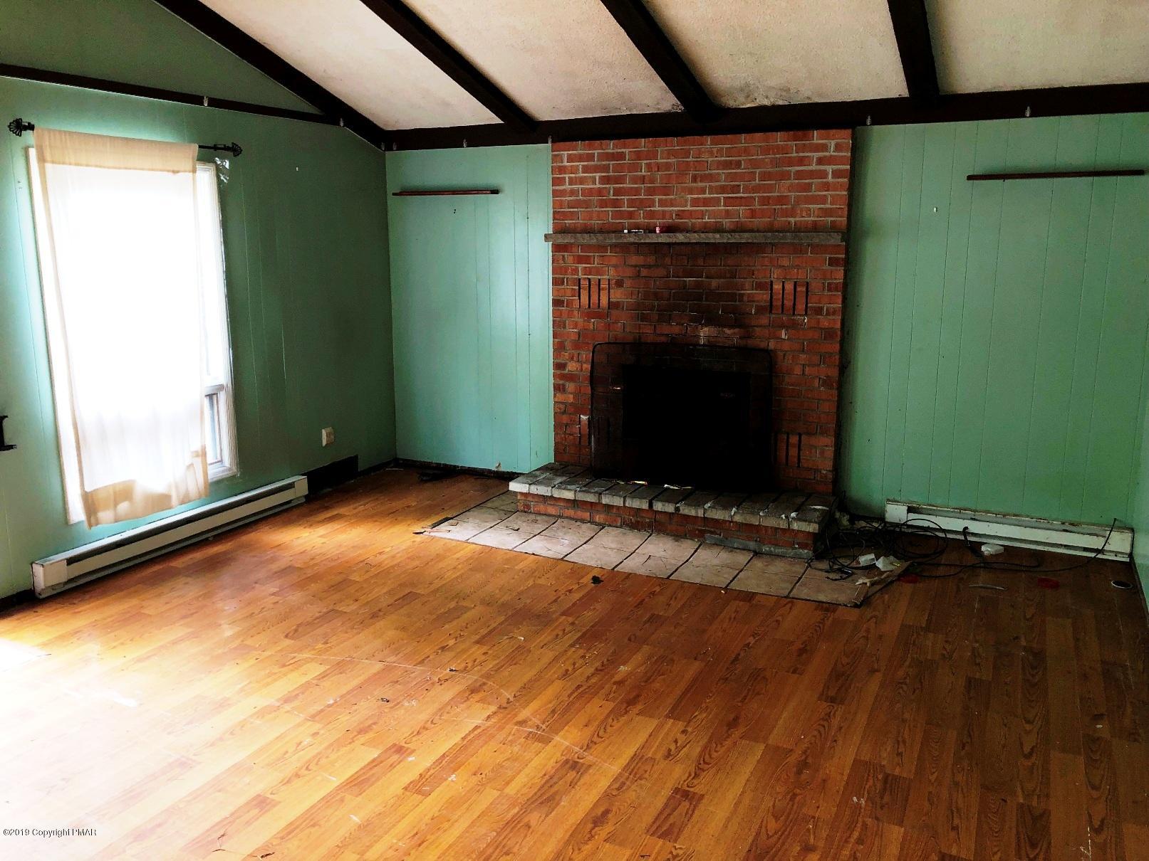 106 Elk Run Road Pocono Lake, PA 18347 - Photo 3 of 11 an empty room with wooden floor and a fireplace