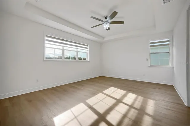 an empty room with wooden floor chandelier fan and windows