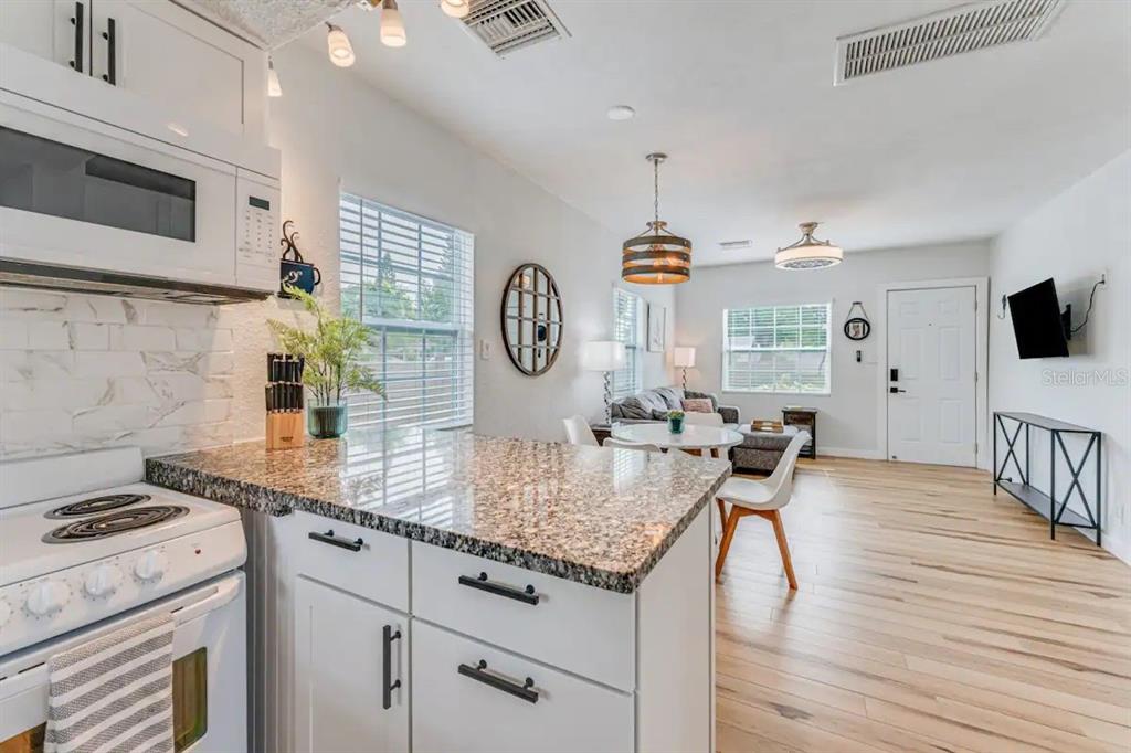 3320 18th Street North St. Petersburg, FL 33713 - Photo 13 of 28 a kitchen with granite countertop a stove a oven a clock and white cabinets with wooden floor