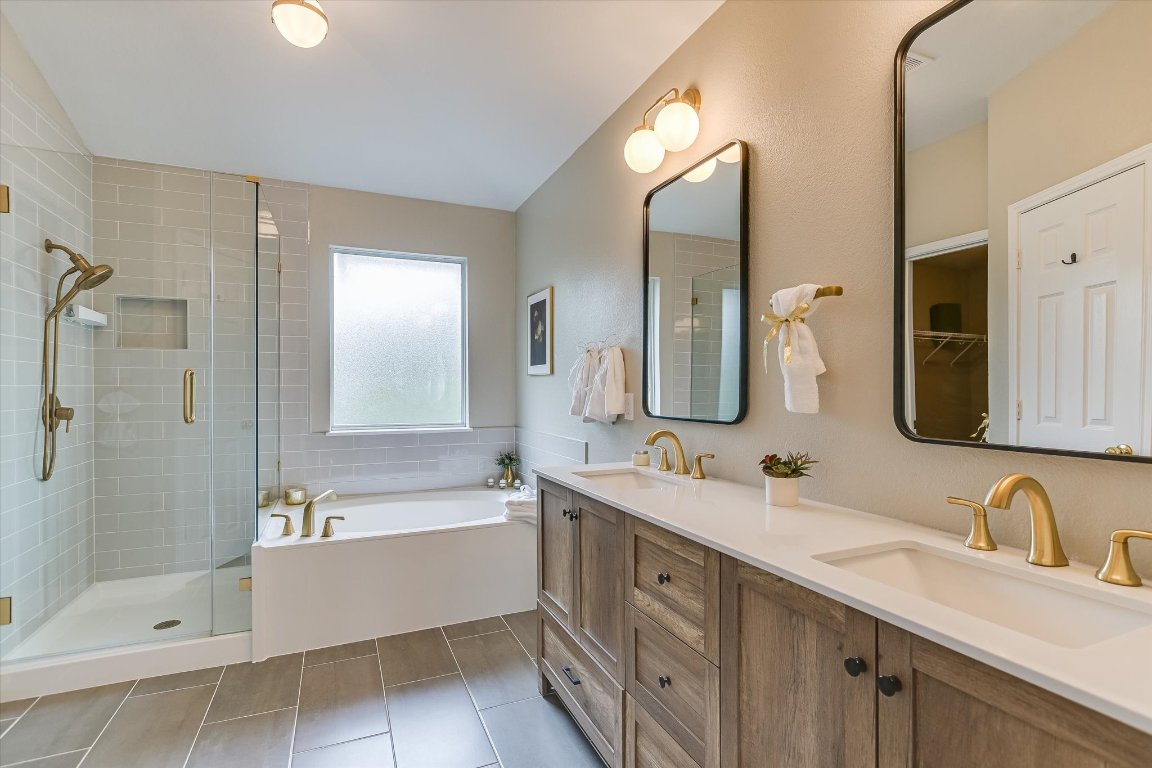 3231 Foothills Trail Round Rock, TX 78681 - Photo 16 of 25 Primary bath has a soaking tub, double vanity, a walk-in shower, gold toned hardware and tile patterned floors with tiled tub and shower surround.
