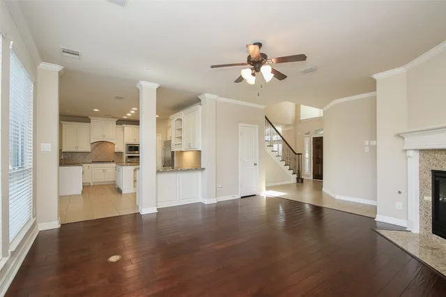 a view of an empty room and a kitchen with wooden floor
