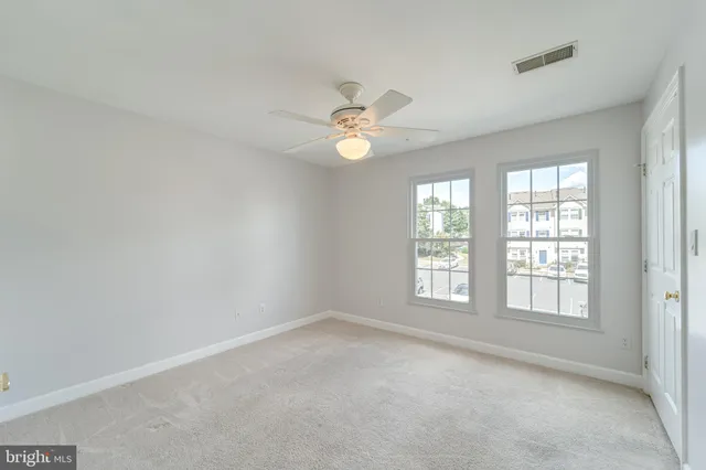 an empty room with chandelier fan and windows