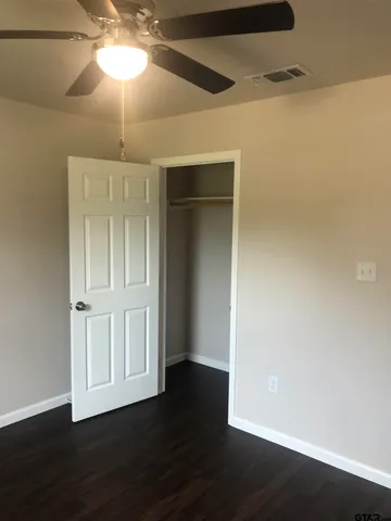 an empty room with wooden floor fan and windows