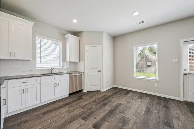 a large white kitchen with granite countertop white cabinets large window and stainless steel appliances