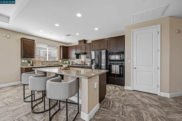 a kitchen with stainless steel appliances granite countertop a stove a sink a refrigerator and chairs