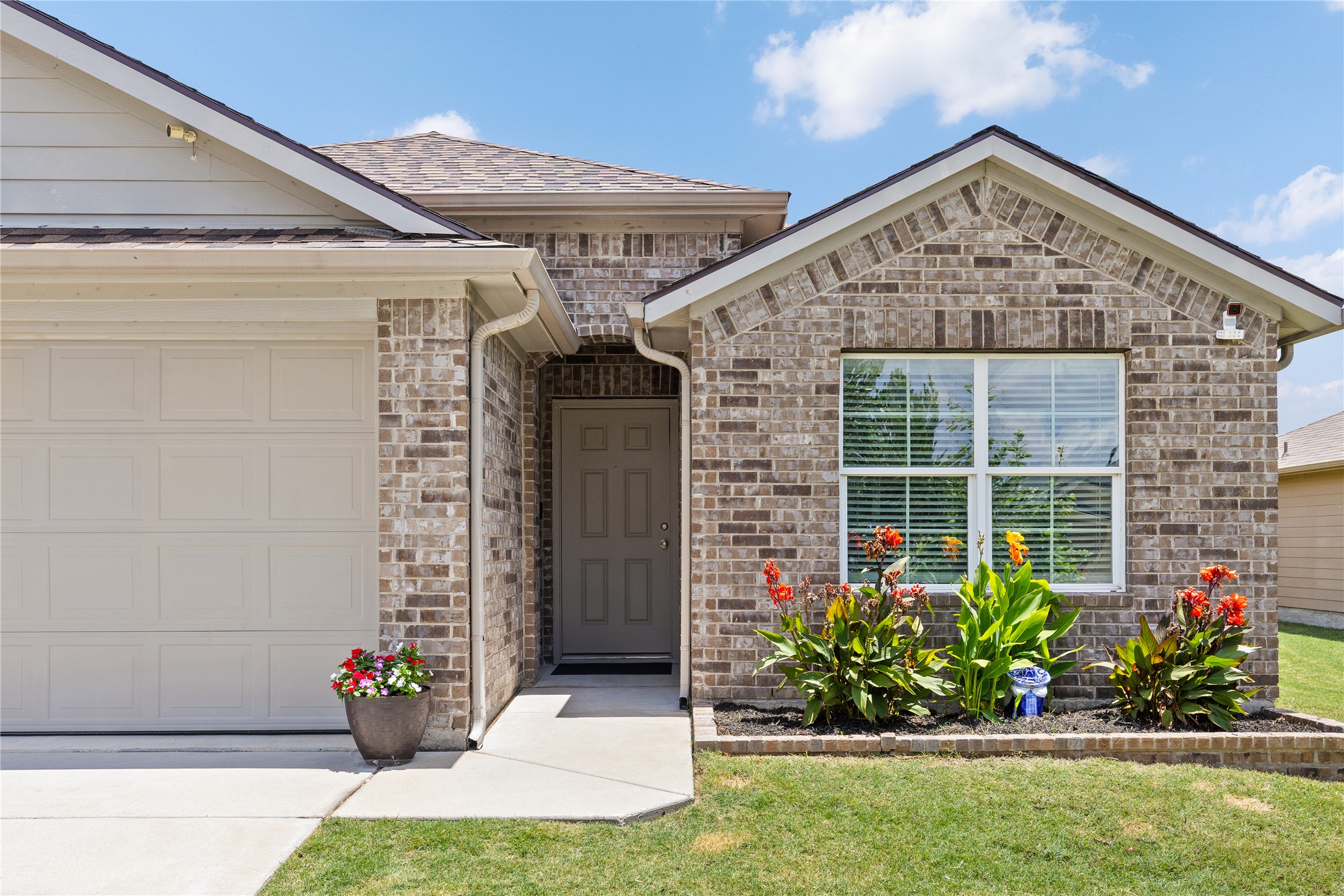 256 Alpha Kyle, TX 78640 - Photo 2 of 27 A welcoming brick facade with lush landscaping and a functional garage door provides attractive curb appeal.
