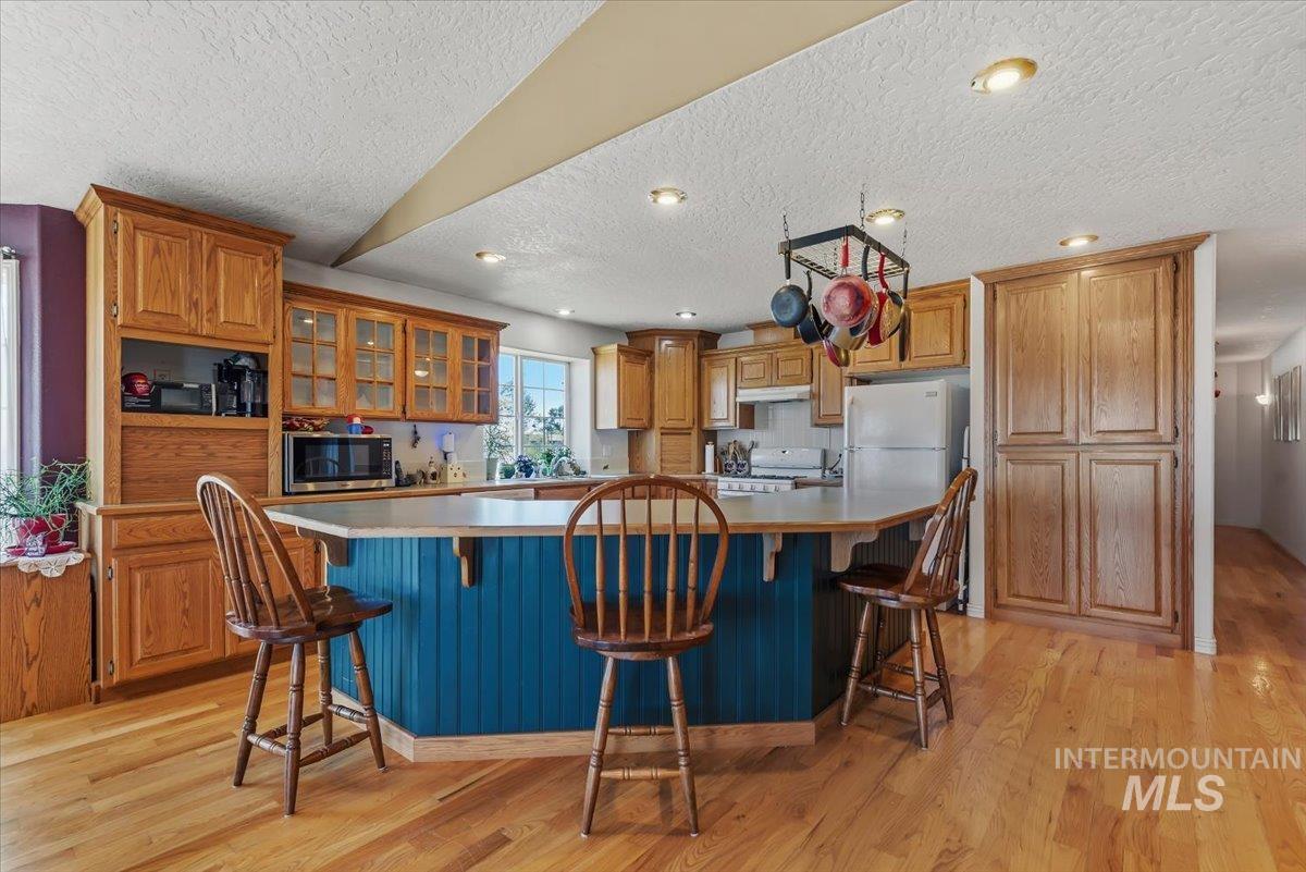 2331 Gulley Road Homedale, ID 83628 - Photo 12 of 46 Kitchen featuring wood-finish flooring, natural wood cabinetry, a central island with a blue beadboard base and light-toned countertop, recessed lighting, and a built-in pantry