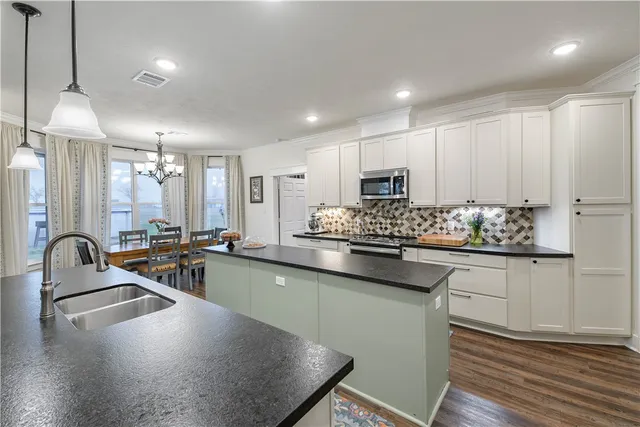 a kitchen with kitchen island stainless steel appliances a dining table chairs sink and cabinets