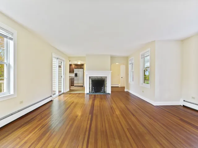 a view of an empty room with wooden floor fireplace and a window