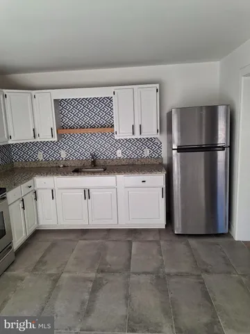 a kitchen with granite countertop a refrigerator a sink and white cabinets