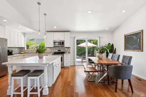 a kitchen with stainless steel appliances granite countertop a stove a refrigerator a kitchen island a dining table and chairs with wooden floor