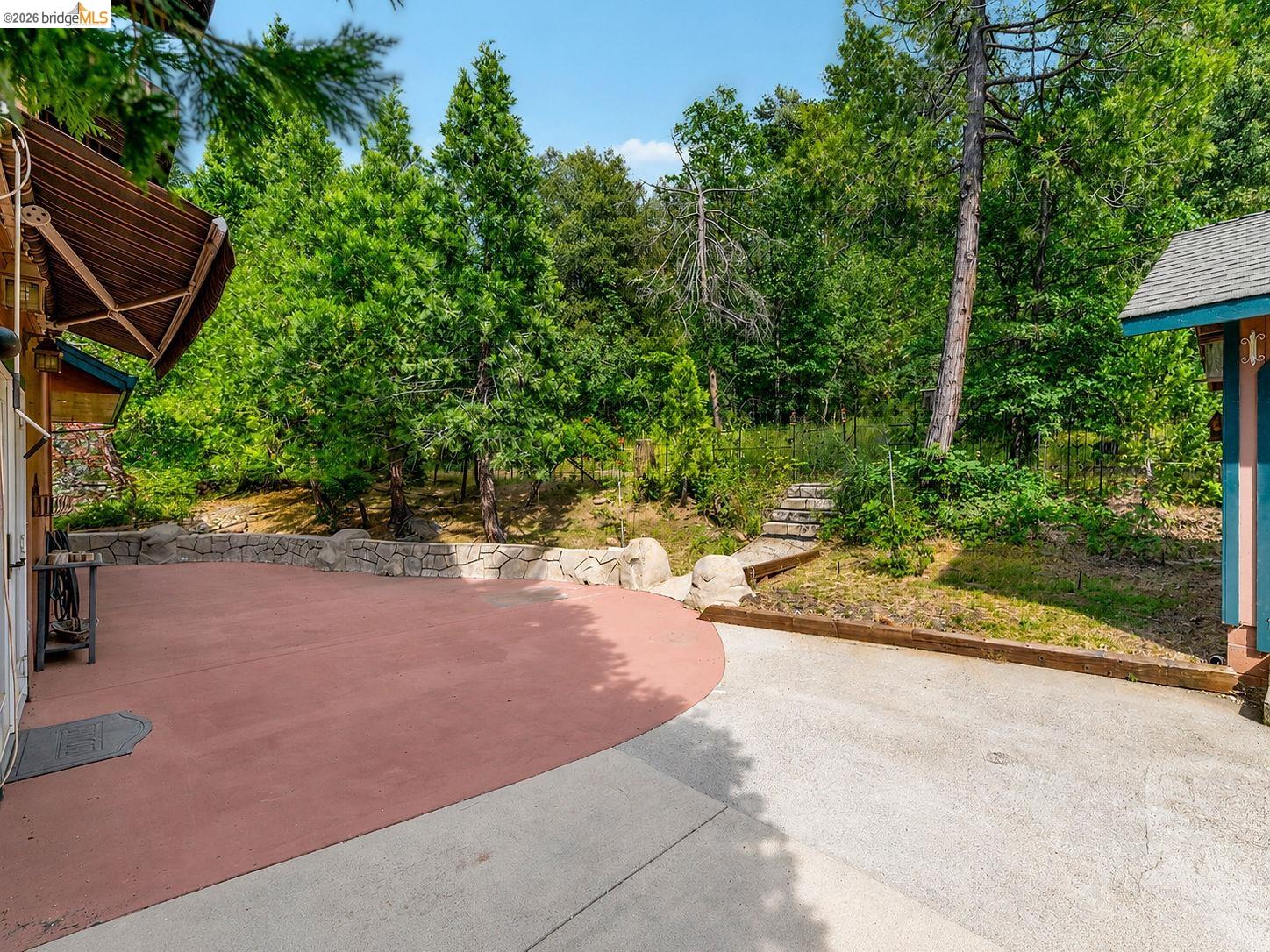 22401 Ridge Road Twain Harte, CA 95383 - Photo 37 of 56 Expansive concrete patio with a red-hued section, framed by a stone retaining wall and mature trees
