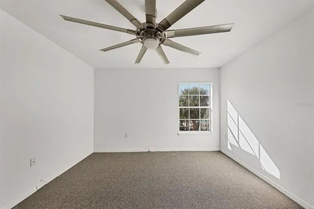 an empty room with chandelier fan and windows