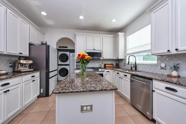 a kitchen with kitchen island granite countertop stainless steel appliances a sink a stove a microwave a refrigerator and cabinets