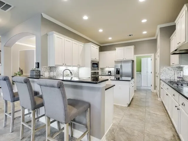 a kitchen with stainless steel appliances granite countertop a stove top oven a sink a refrigerator and white cabinets