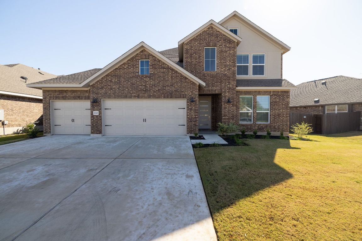Traditional home featuring brick siding, driveway, a shingled roof, and a garage
