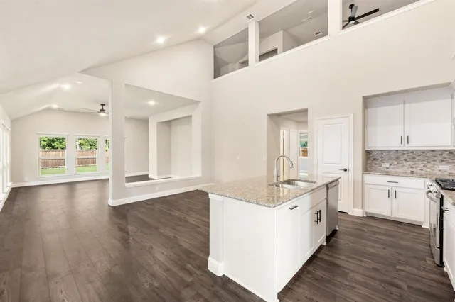 a large white kitchen with granite countertop a stove top oven a sink a chimney wooden floor and cabinets