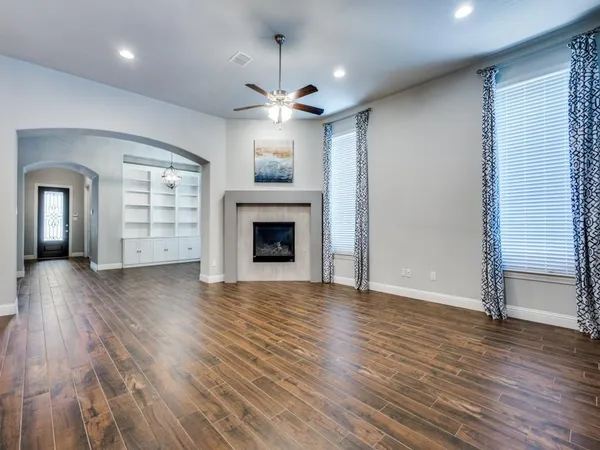 an empty room with wooden floor a ceiling fan and kitchen view