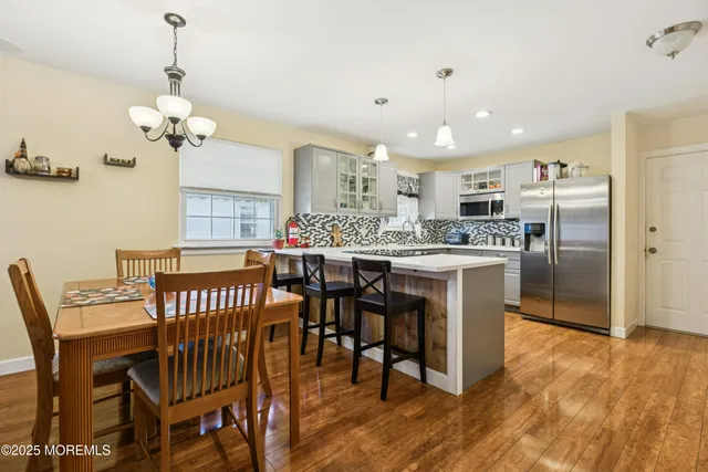 a kitchen with stainless steel appliances kitchen island granite countertop a dining table chairs and a refrigerator