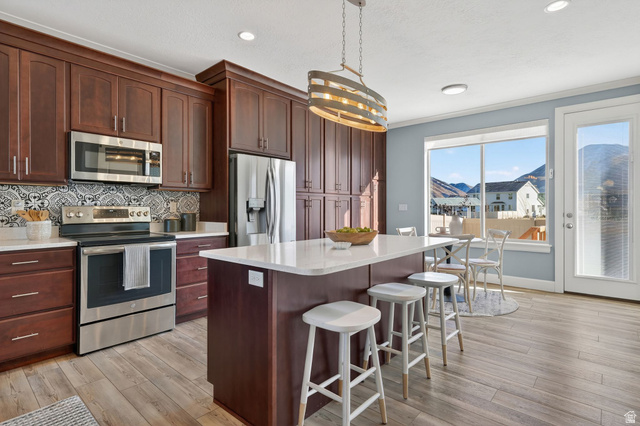 1222 West 190th Street North Mapleton, UT 84664 - Photo 11 of 46 Kitchen featuring extensive dark wood cabinetry, stainless steel appliances, a center island with a white countertop, patterned tile backsplash, and wood-finish flooring