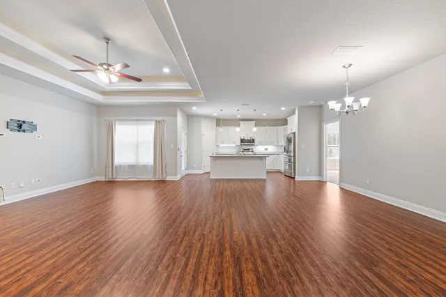 a view of an empty room with wooden floor and kitchen view