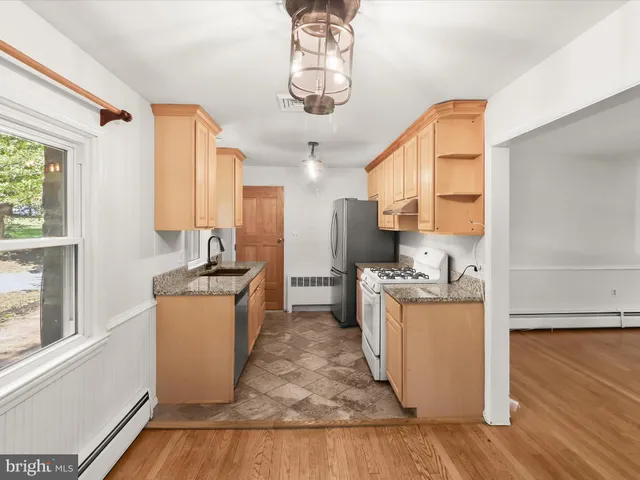 a kitchen with stainless steel appliances granite countertop a refrigerator a stove a sink and white cabinets with wooden floor