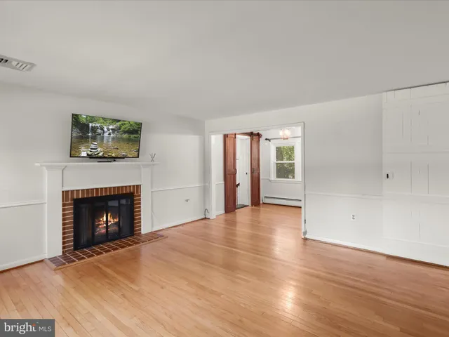 a view of an empty room with wooden floor fireplace and a window