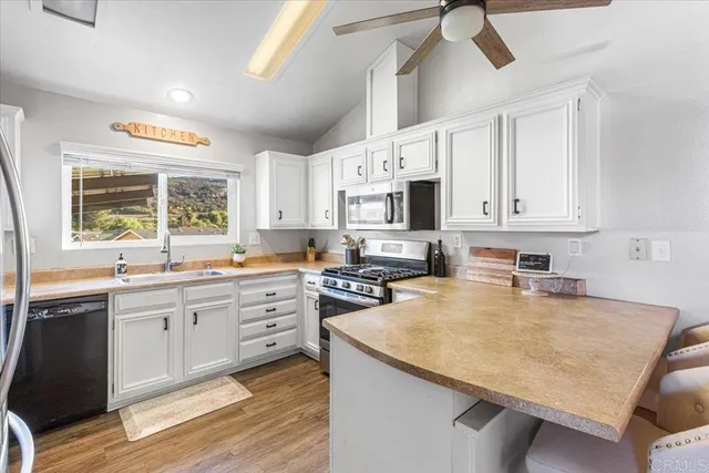 a kitchen with stainless steel appliances granite countertop a sink dishwasher a stove top oven a refrigerator with white cabinets and wooden floor