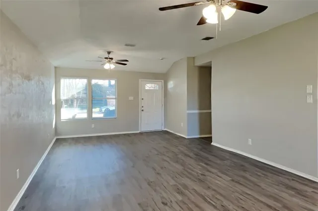 an empty room with wooden floor chandelier fan and windows
