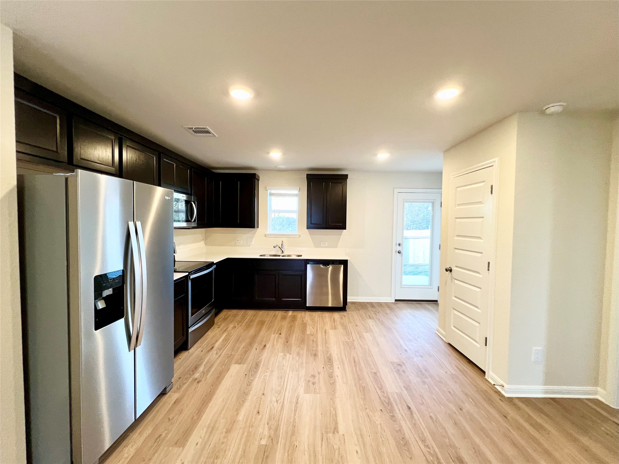 325 Alcatraz Loop Jarrell, TX 76537 - Photo 7 of 16 Kitchen featuring stainless steel appliances, light wood-style floors, recessed lighting, light countertops, and dark cabinets