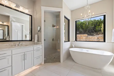 a spacious bathroom with a double vanity sink a large mirror a bathtub and next to a window