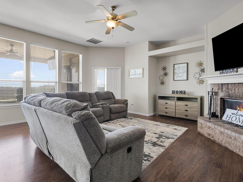 205 King George Road Ponder, TX 76259 - Photo 10 of 37 Wood-finish flooring throughout, light-colored walls, ceiling fan with integrated lighting, brick-faced fireplace with white mantel, built-in wall niche