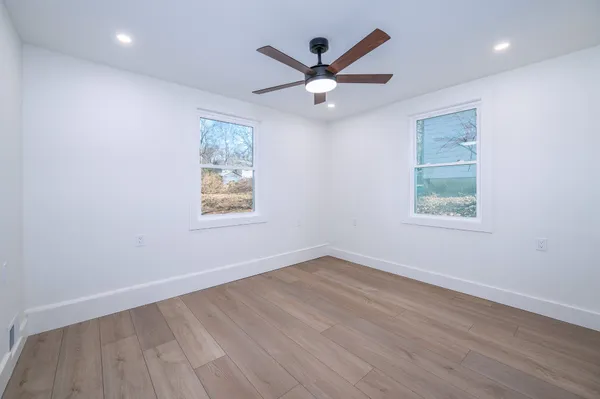 an empty room with wooden floor ceiling fan and windows