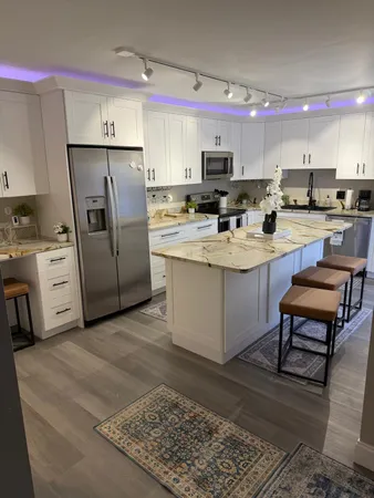 a kitchen with stainless steel appliances kitchen island granite countertop a refrigerator oven a sink dishwasher and white cabinets with wooden floor