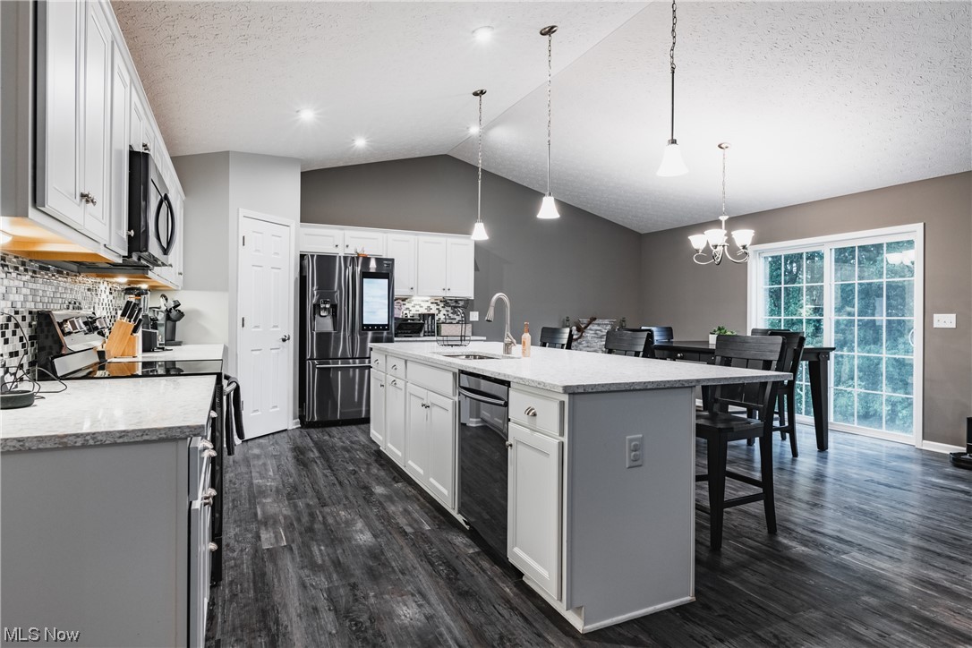 2545 Layman Road Vincent, OH 45784 - Photo 5 of 32 Kitchen with dark hardwood floors, a textured ceiling, decorative light fixtures, backsplash, vaulted ceiling, light countertops, white cabinetry, a center island, and stainless steel appliances