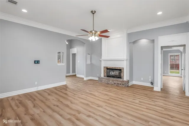 an empty room with wooden floor a chandelier fan and a fireplace