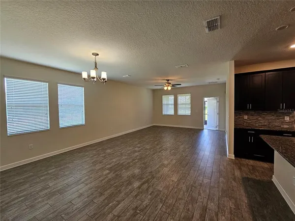 an empty room with wooden floor and kitchen view