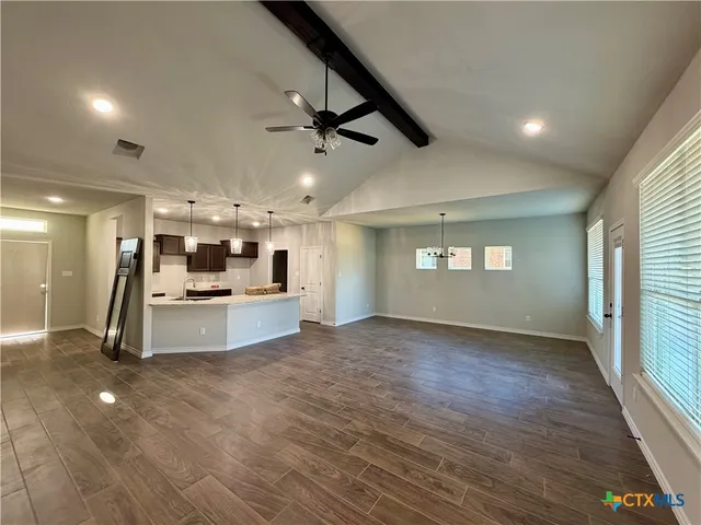 a view of an empty room with kitchen and window