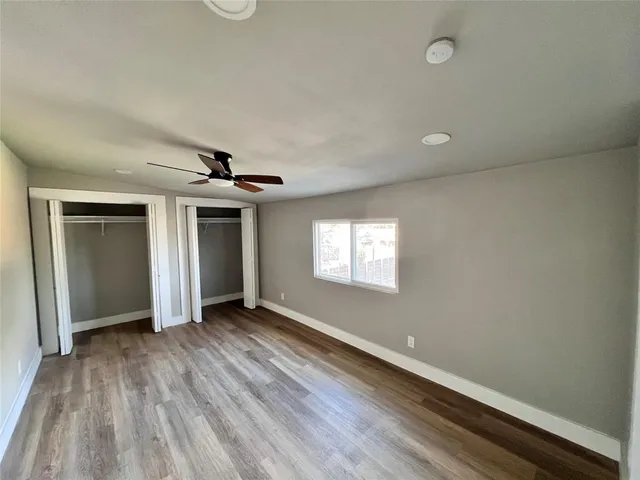 an empty room with wooden floor ceiling fan and windows