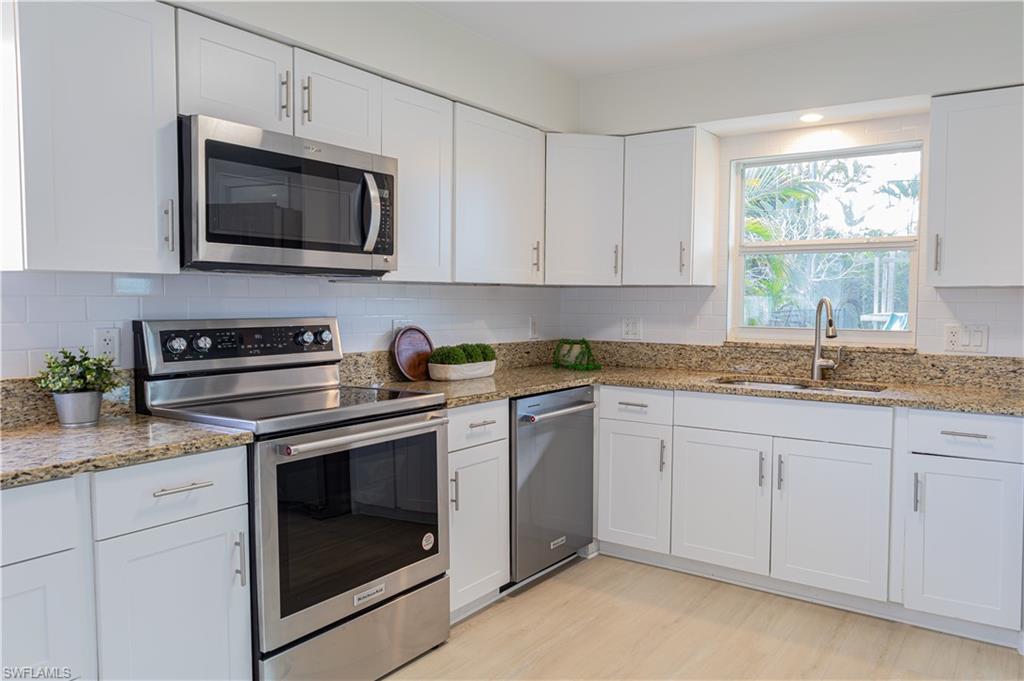 1060 Cooper Drive Naples, FL 34103 - Photo 9 of 24 Kitchen with stainless steel appliances, white cabinetry, light stone counters, and light wood-type flooring