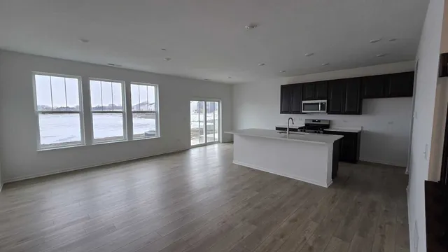 a kitchen with stainless steel appliances a microwave a stove a sink a refrigerator white cabinets and wooden floor