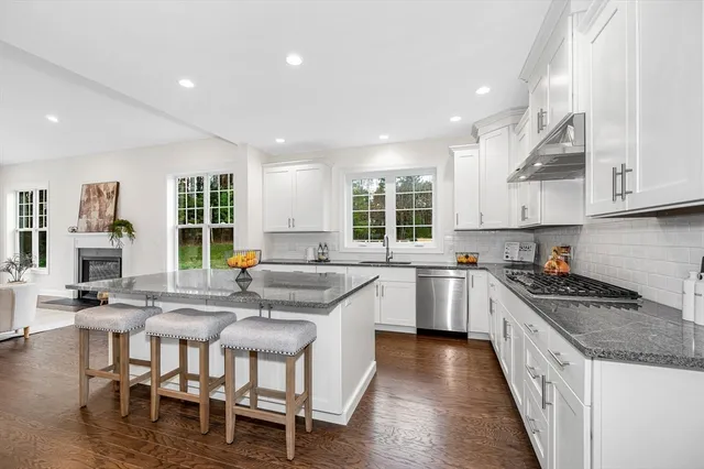 a kitchen with stainless steel appliances granite countertop a stove top oven a sink a refrigerator and white cabinets with wooden floor