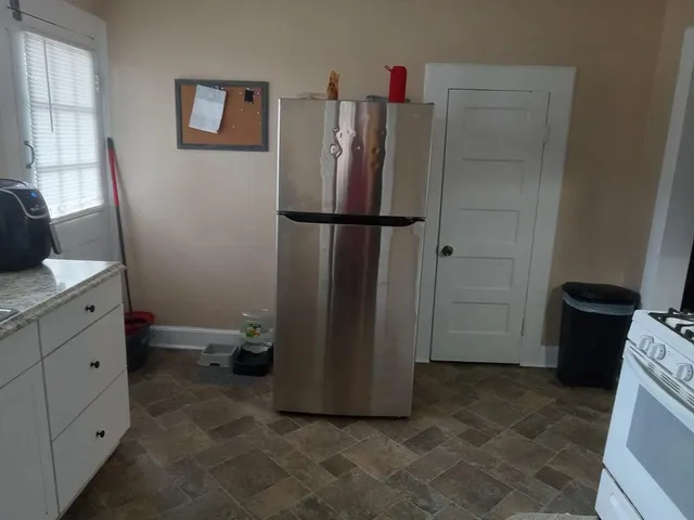 a view of a refrigerator in kitchen and an empty room