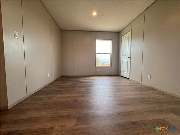 an empty room with wooden floor and windows with curtains