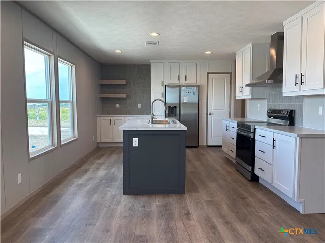 a kitchen with stainless steel appliances granite countertop a stove a sink a refrigerator white cabinets and wooden floor