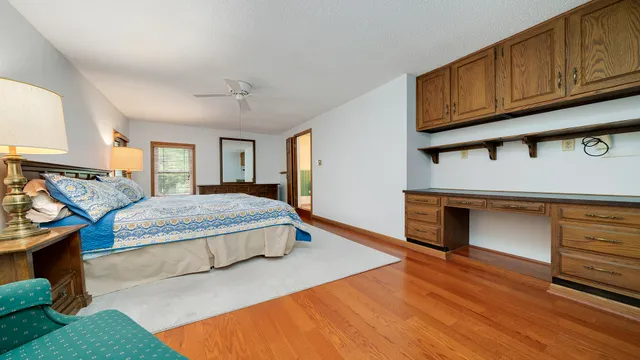 a spacious bedroom with a bed table chair and two windows