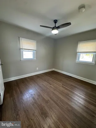 an empty room with wooden floor fan and windows