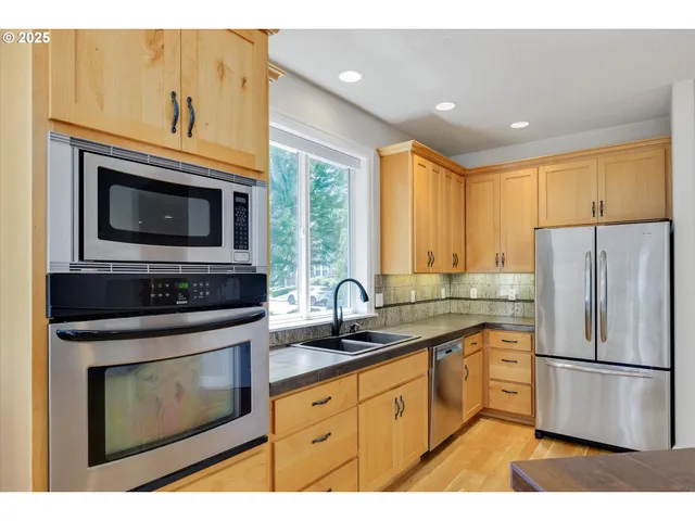 a kitchen with stainless steel appliances a stove a sink a refrigerator cabinets and a window