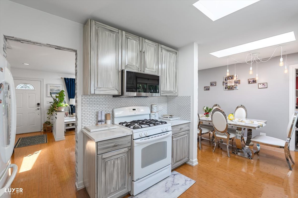 6908 Orchard Lane Hanover Park, IL 60133 - Photo 11 of 28 a kitchen with stainless steel appliances a stove a sink white cabinets a dining table and chairs