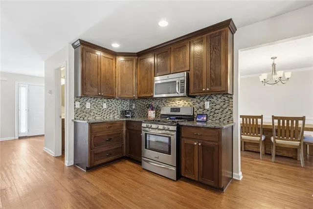 a kitchen with stainless steel appliances granite countertop wooden cabinets a stove a sink and a wooden floors
